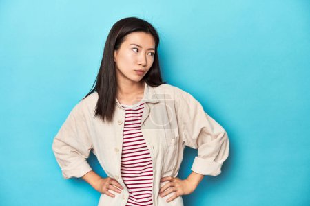 Photo for Asian woman in layered shirt and striped t-shirt, confused, feels doubtful and unsure. - Royalty Free Image
