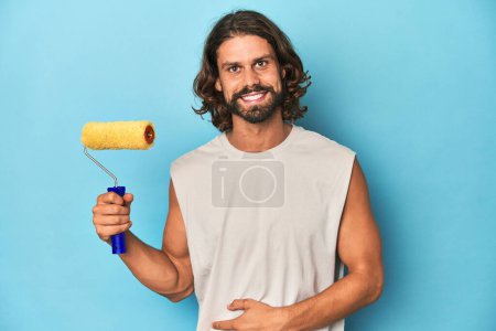 Photo for Bearded man painting with a yellow roller laughing and having fun. - Royalty Free Image