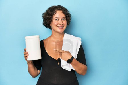 Photo for Young sportswoman with protein shake smiling and pointing aside, showing something at blank space. - Royalty Free Image