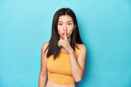 Photo for Asian woman in summer yellow top, studio setup, keeping a secret or asking for silence. - Royalty Free Image
