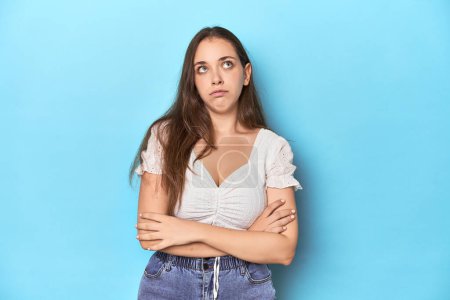 Photo for Stylish young woman in white blouse on a blue studio backdrop tired of a repetitive task. - Royalty Free Image