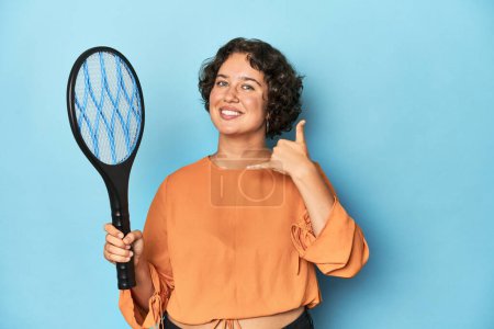 Photo for Young woman with electric mosquito racket Young woman with electric mosquito racketshowing a mobile phone call gesture with fingers. - Royalty Free Image