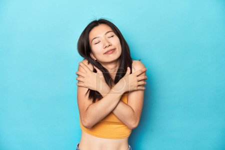Foto de Mujer asiática en la parte superior amarilla de verano, configuración del estudio, abrazos, sonriendo despreocupado y feliz. - Imagen libre de derechos