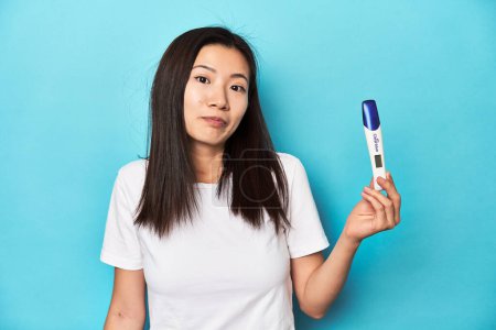 Foto de Joven mujer asiática sosteniendo una prueba de embarazo, estudio de tiro. - Imagen libre de derechos
