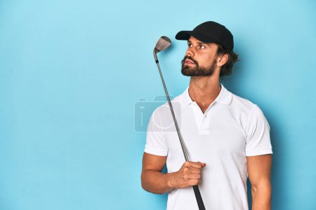 Foto de Golfista barbudo de pelo largo sosteniendo un club de golf en un estudio azul. - Imagen libre de derechos