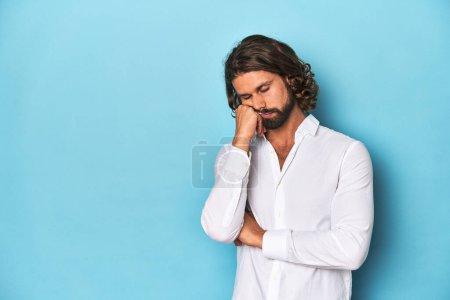 Téléchargez les photos : Homme barbu dans une chemise blanche, fond bleu qui se sent triste et coûteux, regardant l'espace de copie. - en image libre de droit