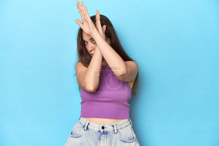 Photo for Fashionable young woman in a purple top on blue background keeping two arms crossed, denial concept. - Royalty Free Image