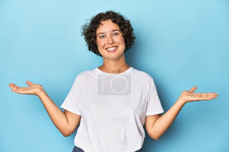 Photo for Young Caucasian woman with short hair makes scale with arms, feels happy and confident. - Royalty Free Image