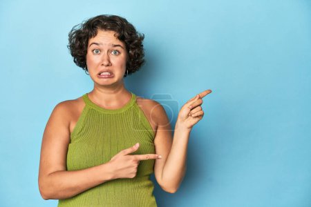 Photo for Young Caucasian woman with short hair shocked pointing with index fingers to a copy space. - Royalty Free Image