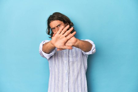 Photo for Man with beard in blue striped shirt, blue studio doing a denial gesture - Royalty Free Image