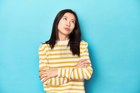 Photo for Asian woman in striped yellow sweater, tired of a repetitive task. - Royalty Free Image