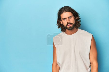 Photo for Bearded man in a tank top, blue backdrop shouting very angry, rage concept, frustrated. - Royalty Free Image