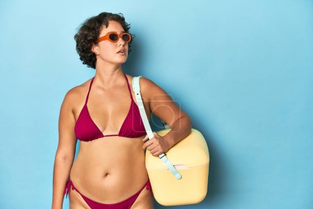 Foto de Joven mujer caucásica en bikini sosteniendo un enfriador de playa, toma de estudio. - Imagen libre de derechos