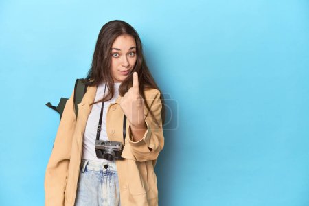 Foto de Joven mujer caucásica viajero con cámara y mochila apuntando con el dedo a usted como si invitando a acercarse. - Imagen libre de derechos