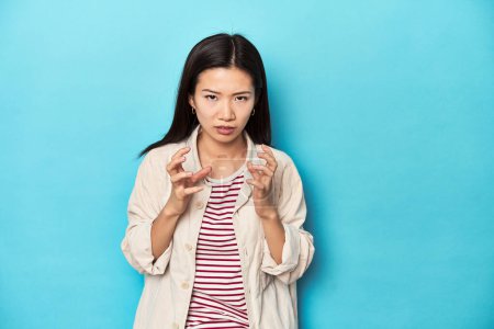 Photo for Asian woman in layered shirt and striped t-shirt, upset screaming with tense hands. - Royalty Free Image