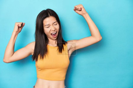 Téléchargez les photos : Femme asiatique en haut jaune d'été, installation de studio, levant le poing après une victoire, concept gagnant. - en image libre de droit