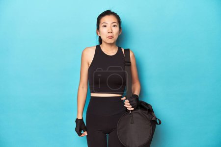 Photo for Asian woman with gym gear, ready for workout session, shrugs shoulders and open eyes confused. - Royalty Free Image