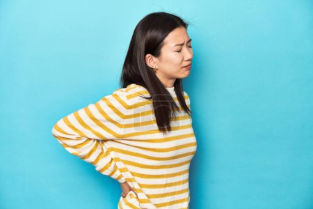 Photo for Asian woman in striped yellow sweater, suffering a back pain. - Royalty Free Image