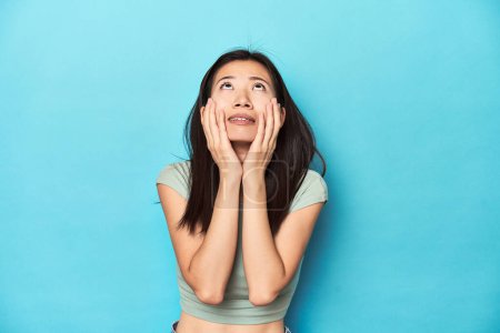 Photo for Asian woman in summer green top, studio backdrop, whining and crying disconsolately. - Royalty Free Image
