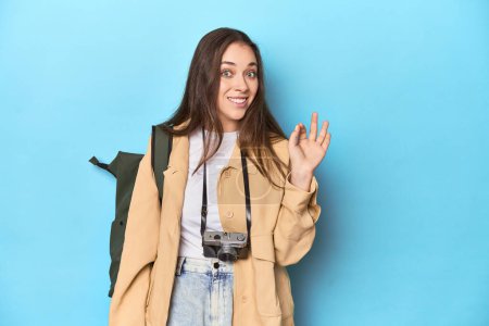 Photo for Young Caucasian woman traveler with camera and backpack cheerful and confident showing ok gesture. - Royalty Free Image