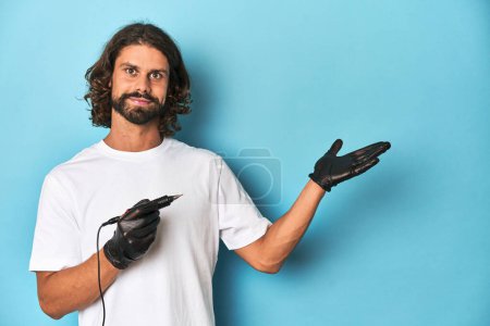 Photo for Bearded tattooist holding a tattoo machine in a blue studio. - Royalty Free Image