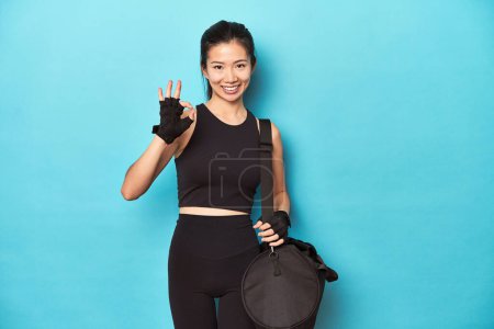 Photo for Asian woman with gym gear, ready for workout session, cheerful and confident showing ok gesture. - Royalty Free Image