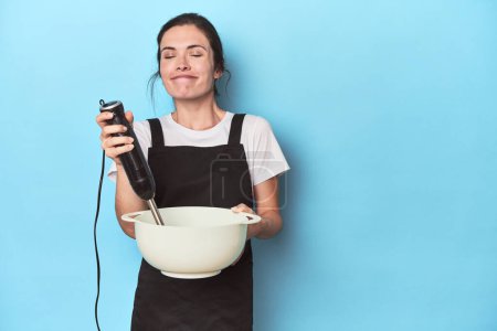 Téléchargez les photos : Jeune chef avec mélangeur préparant une pâte sur bleu - en image libre de droit