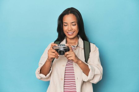 Photo for Young Filipina capturing moments with camera on a blue studio backdrop - Royalty Free Image