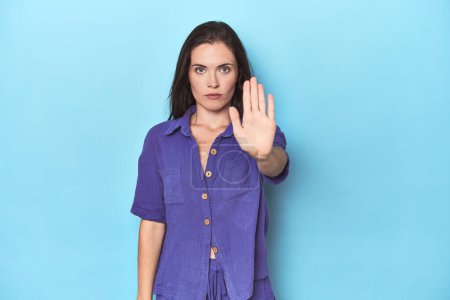 Photo for Young caucasian woman on blue backdrop standing with outstretched hand showing stop sign, preventing you. - Royalty Free Image