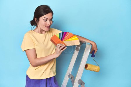 Photo for Woman with color palette painting wall on ladder - Royalty Free Image