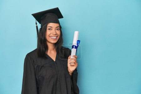 Foto de Celebrando Filipina graduado con diploma y gorra en estudio azul - Imagen libre de derechos