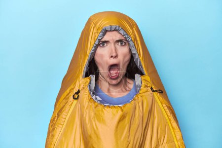 Photo for Woman in sleeping bag on blue background screaming very angry and aggressive. - Royalty Free Image