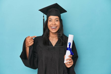 Photo for Celebrating Filipina graduate with diploma and cap on blue studio - Royalty Free Image