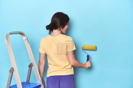 Foto de Mujer pintando una pared azul desde una escalera - Imagen libre de derechos