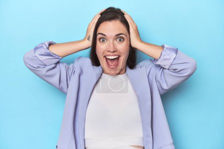 Photo for Woman in blue blazer on blue background screaming, very excited, passionate, satisfied with something. - Royalty Free Image