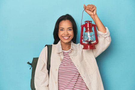 Photo for Young Filipina traveler holding a vintage lantern on blue backdrop - Royalty Free Image