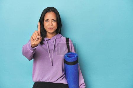 Foto de Atleta filipina con esterilla de yoga en azul mostrando el número uno con el dedo. - Imagen libre de derechos
