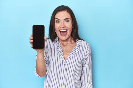Téléchargez les photos : Femme pleine d'espoir affichant écran de téléphone sur bleu - en image libre de droit