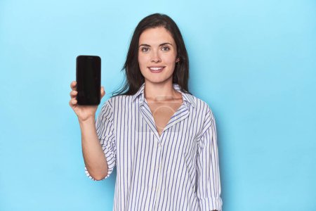 Téléchargez les photos : Femme affichant l'écran de téléphone sur fond bleu - en image libre de droit