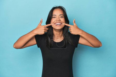 Téléchargez les photos : Philippine jeune femme sur bleu studio sourit, les doigts pointant vers la bouche. - en image libre de droit