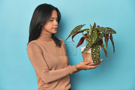 Photo for Young Filipina holding a green plant on blue studio backdrop - Royalty Free Image