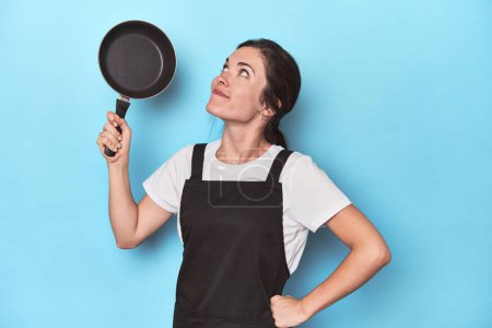 Photo for Confident young chef with pan, playful attitude on blue - Royalty Free Image