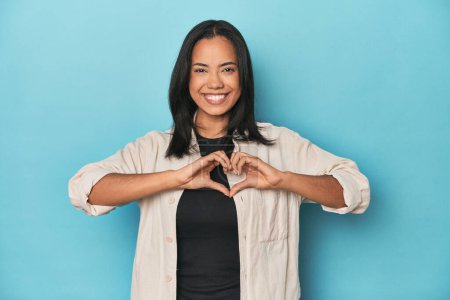 Téléchargez les photos : Philippine jeune femme sur studio bleu souriant et montrant une forme de coeur avec les mains. - en image libre de droit