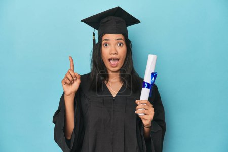 Photo for Filipina graduate with diploma on blue studio having an idea, inspiration concept. - Royalty Free Image