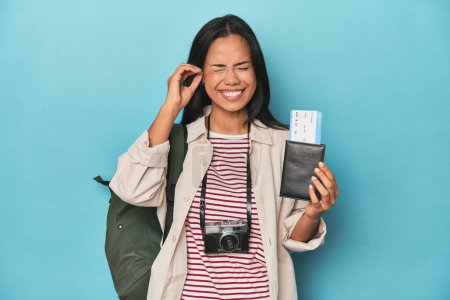 Téléchargez les photos : Filipina avec appareil photo, billets, sac à dos sur les oreilles de couverture bleu avec les mains. - en image libre de droit