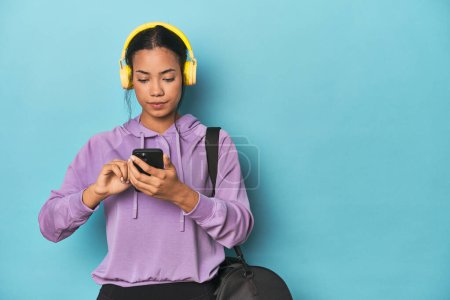 Photo for Filipina athlete with phone and headphones on blue studio background - Royalty Free Image