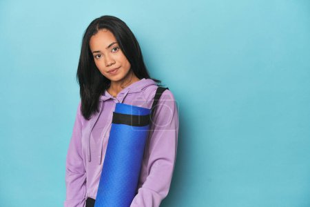 Téléchargez les photos : Athlète philippin posant avec un tapis de yoga sur fond bleu studio - en image libre de droit