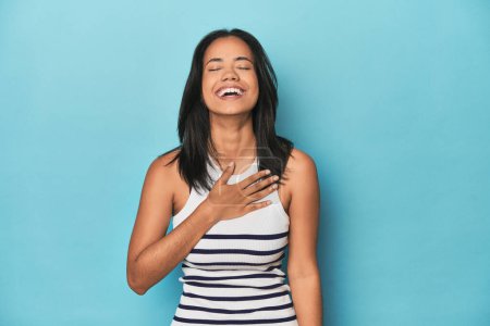 Photo for Filipina young woman on blue studio laughs out loudly keeping hand on chest. - Royalty Free Image