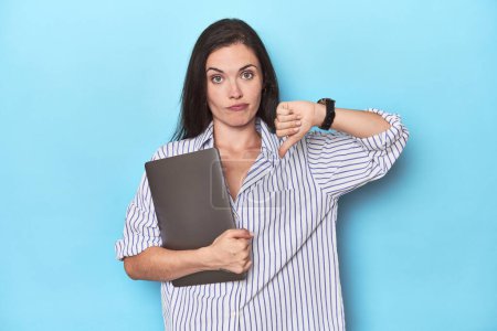 Foto de Joven mujer de negocios sosteniendo el portátil en azul mostrando un gesto de aversión, pulgares hacia abajo. Concepto de desacuerdo. - Imagen libre de derechos