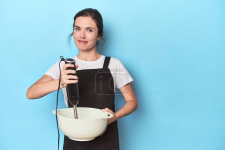 Foto de Joven chef con batidora preparando una masa en azul - Imagen libre de derechos